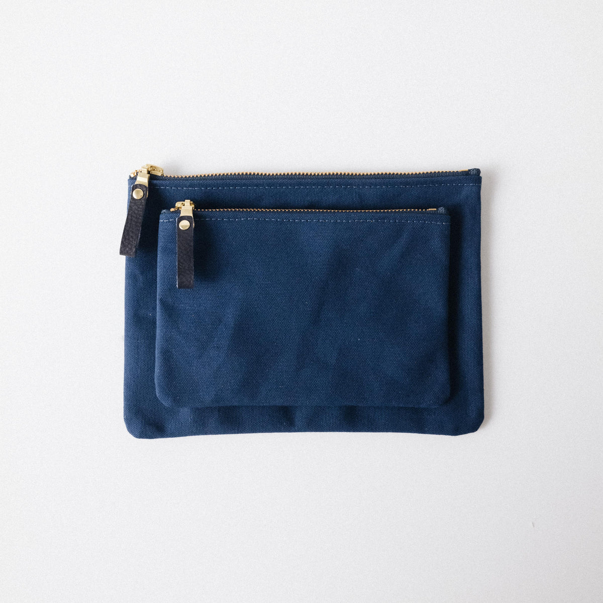 Two navy blue heavyweight cotton canvas zip pouches with solid brass zippers and leather pulls.
