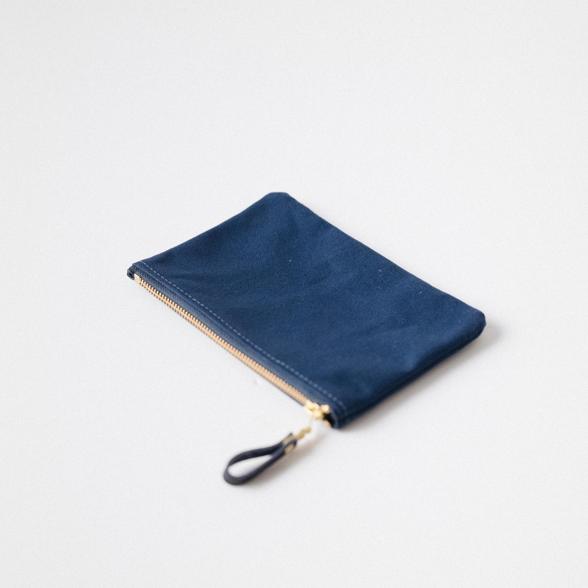 Navy blue heavyweight cotton canvas zip pouch with a solid brass zipper and matching leather pull.
