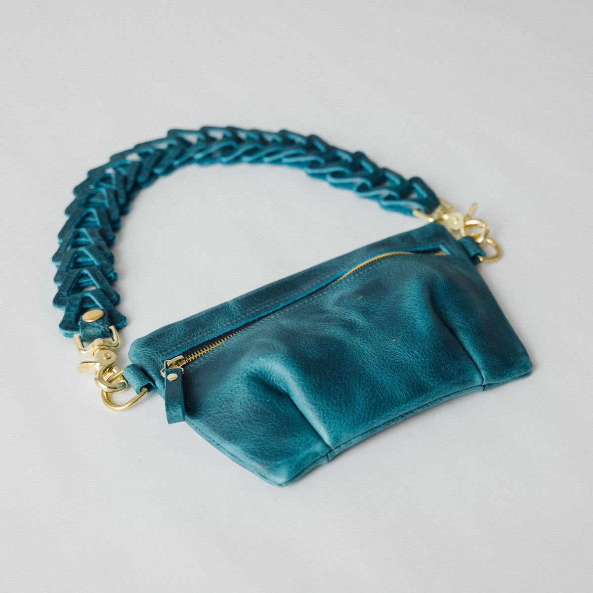 Petrol blue bison leather belt bag with a pleated design, brass zipper, and adjustable leather chain link strap.