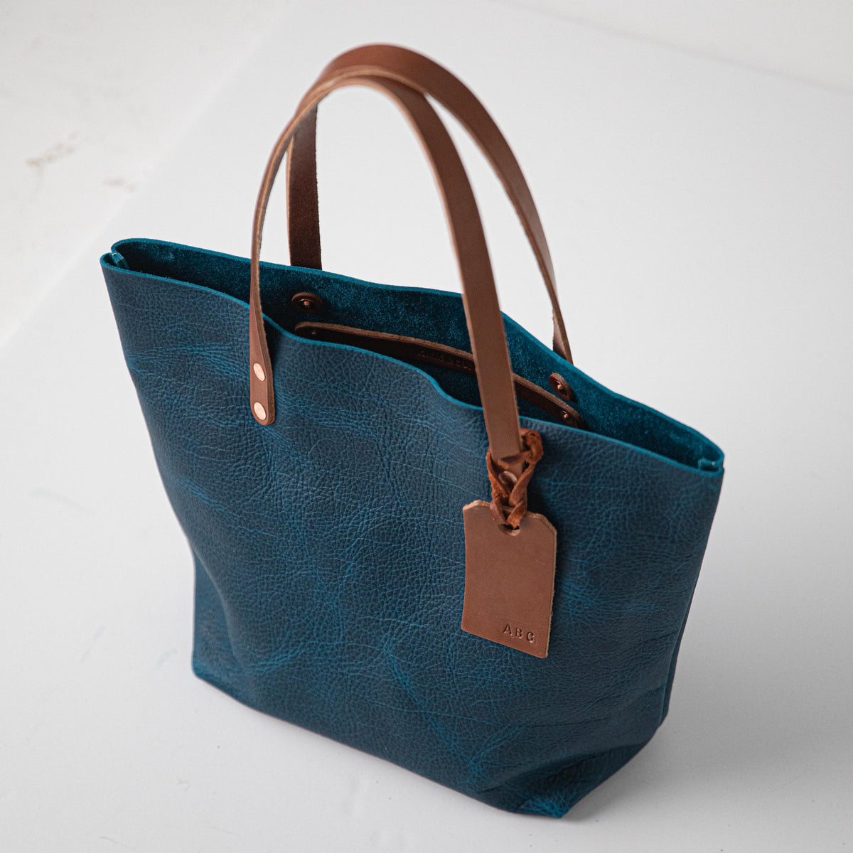 Handmade Petrol Blue Bison leather tote bag featuring a rich natural grain, durable tan handles, and a custom embossed tag.
