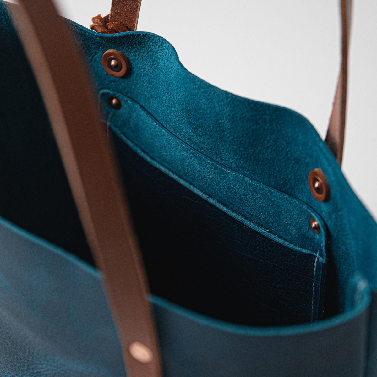 Petrol Blue Bison leather tote featuring a vibrant blue grain, sturdy tan leather handles, and secure copper-toned rivets.