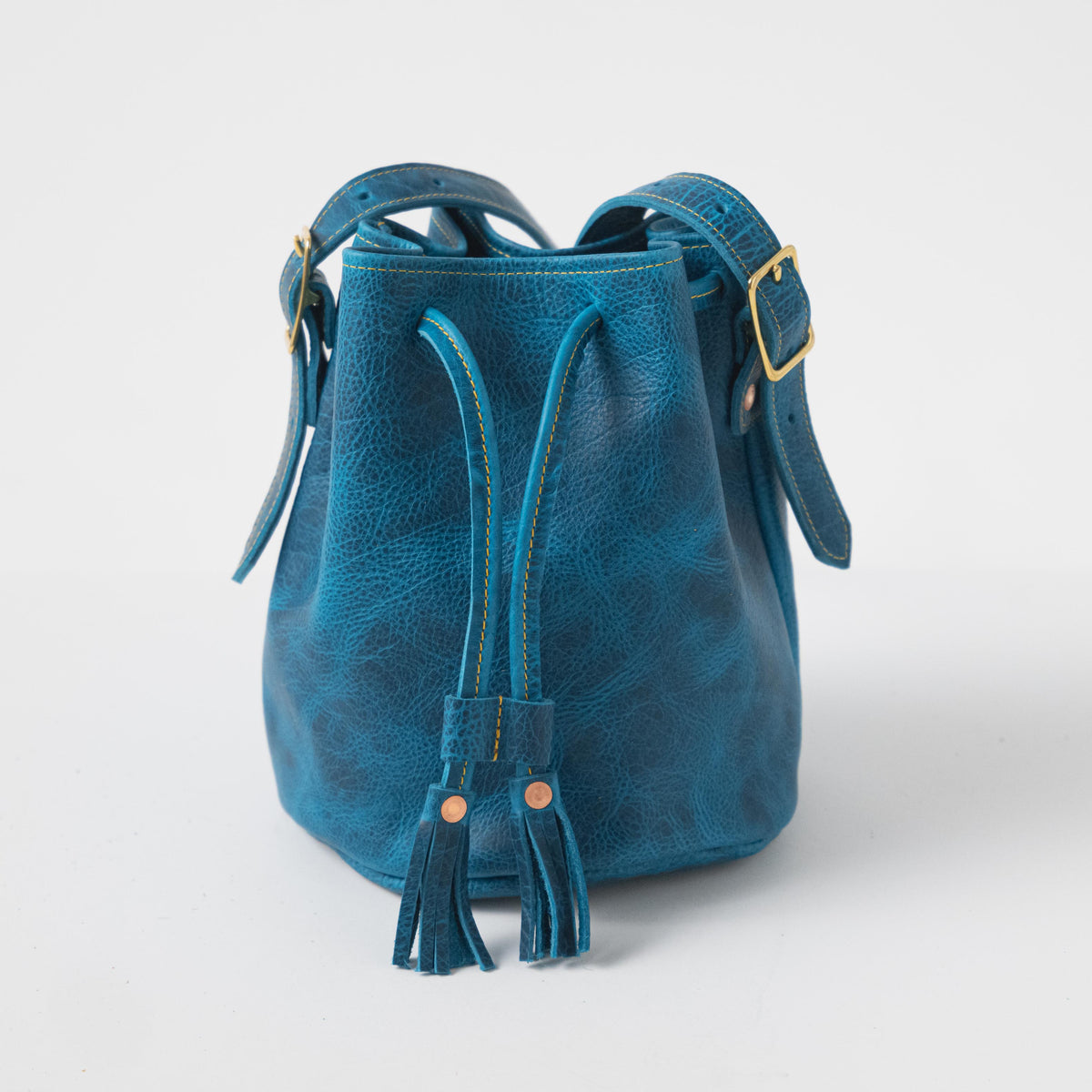 Petrol Blue Bison Bucket Bag: textured leather, drawstring closure with playful tassels, adjustable strap, brass hardware.