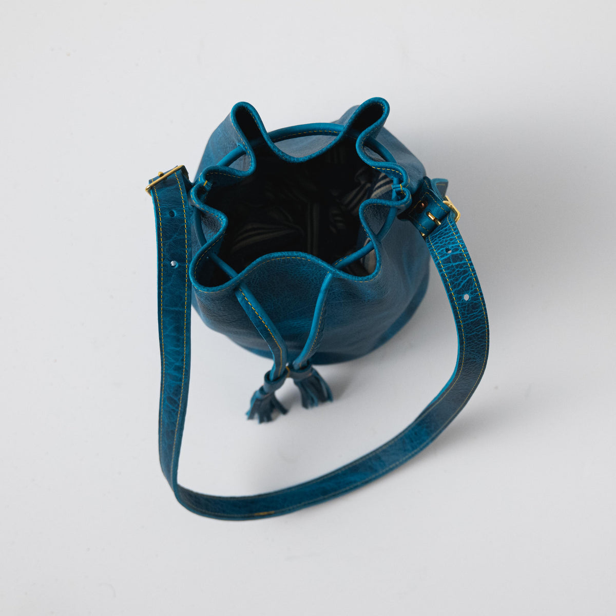 Petrol Blue Bison Bucket Bag: classic leather silhouette with drawstring closure, playful tassels, and adjustable strap.