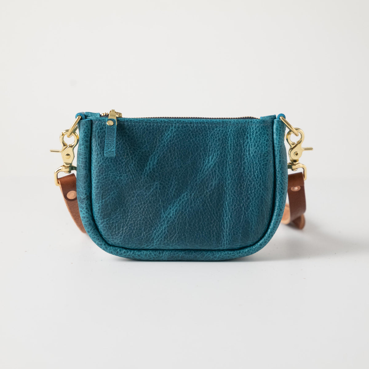 Petrol blue full-grain leather mini crossbody bag with solid brass hardware and a secure top zipper.