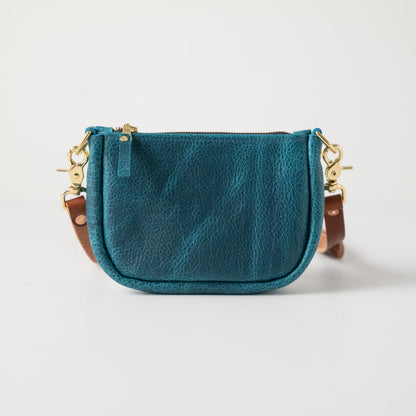 Petrol blue full-grain leather mini crossbody bag with solid brass hardware and a secure top zipper.