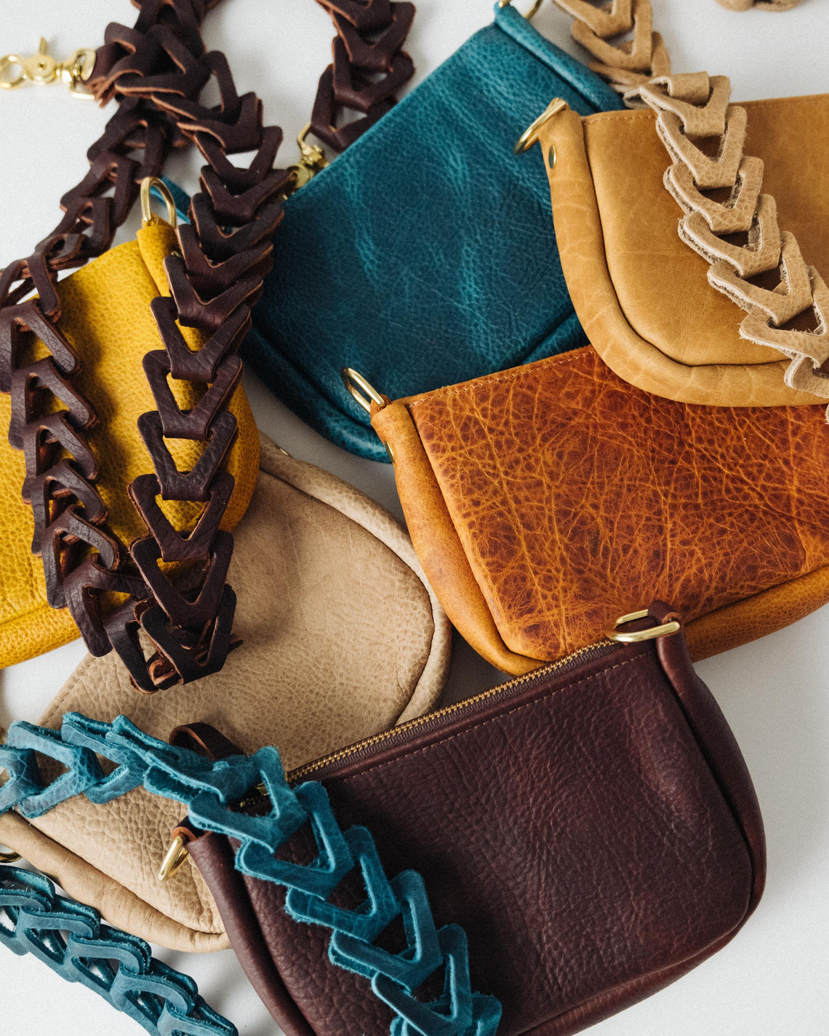 Handmade full-grain leather mini crossbody bags in assorted colors with solid brass zippers and decorative chain straps.