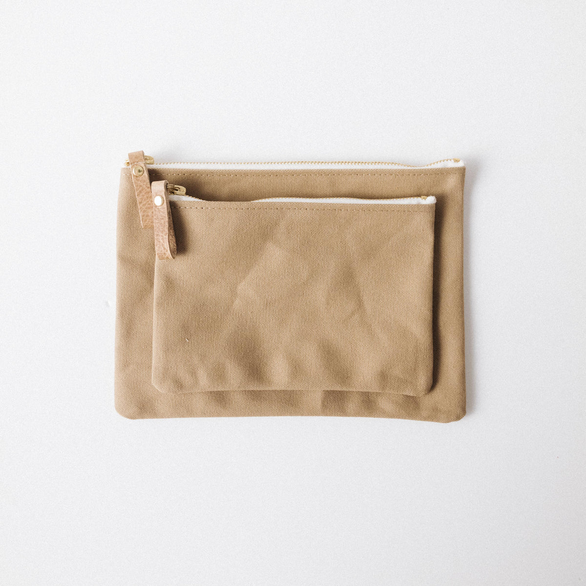 Two handmade tan cotton canvas zip pouches with solid brass zippers and leather pulls, perfect for organizing your tote.