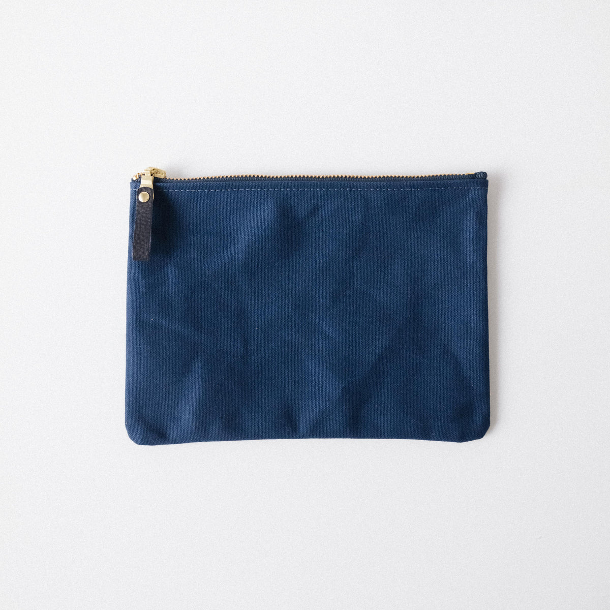 Navy blue heavyweight canvas zip pouch with a solid brass zipper and leather pull for stylish organization.
