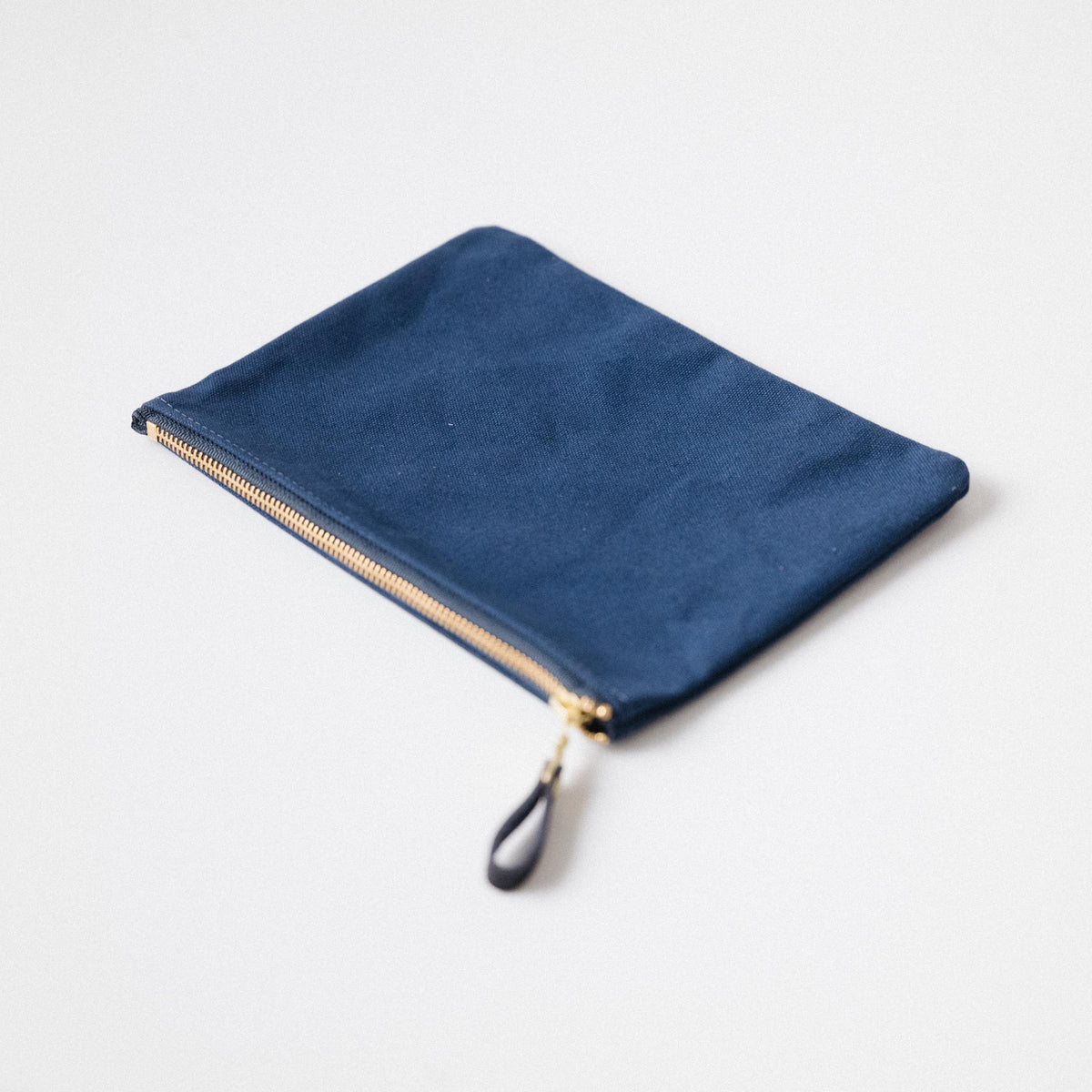 Handmade navy blue heavyweight cotton canvas zip pouch with a solid brass zipper and matching leather pull.