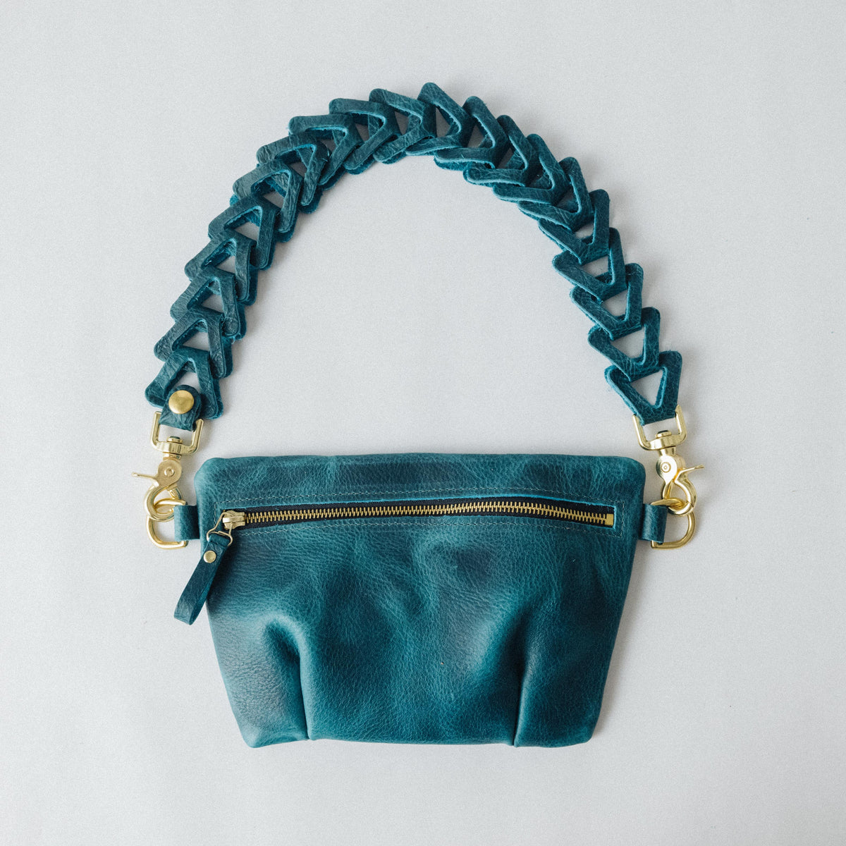 Petrol blue bison leather belt bag with a pleated design, brass zipper, and adjustable leather chain link strap.