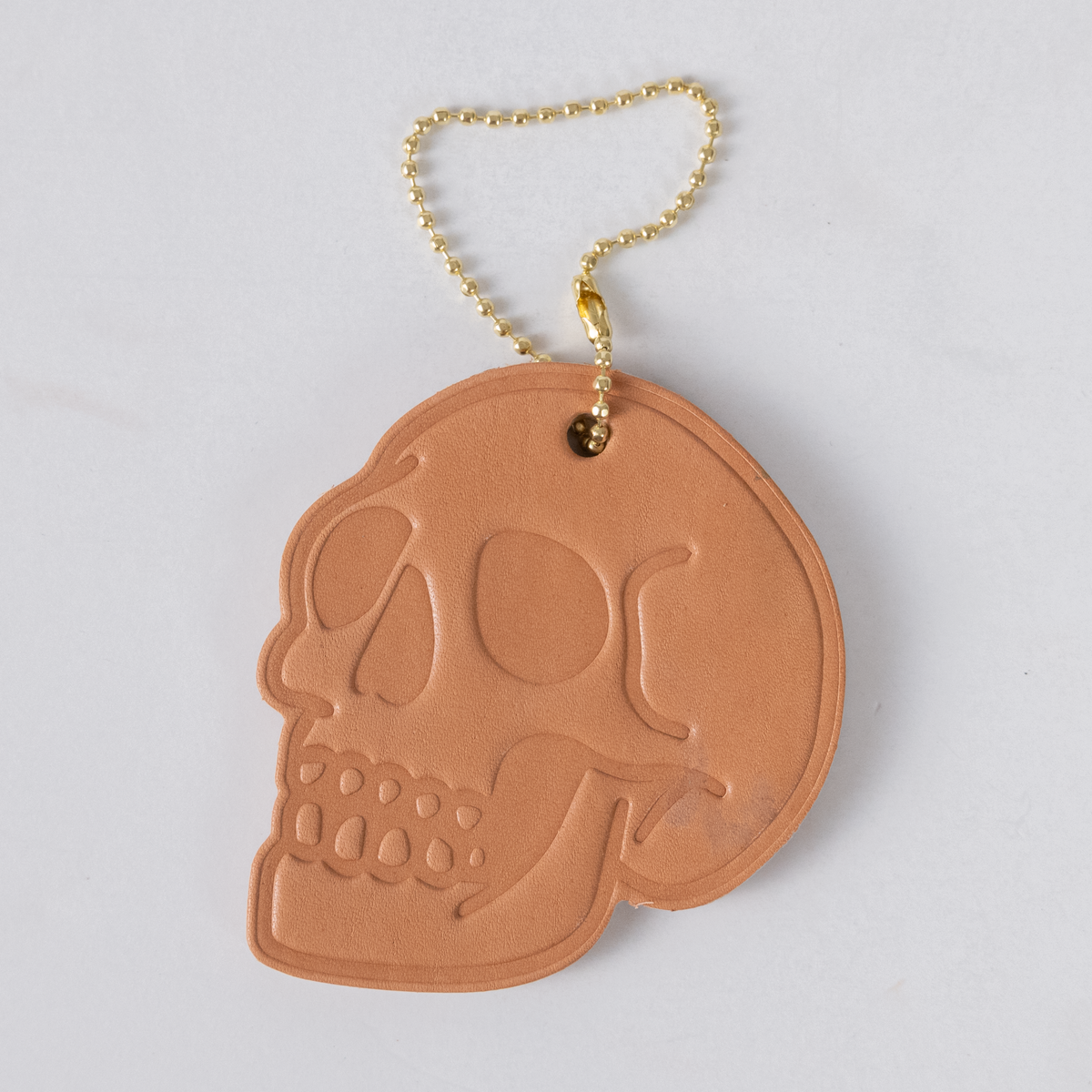 Natural Essex 2-ply leather skull tag with embossed detail and a brass ball chain for easy bag attachment.