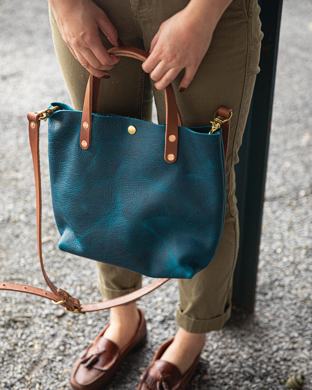 Petrol Blue Bison Mini Tote, a vibrant blue full-grain leather bag with Tan handles, held by a person.