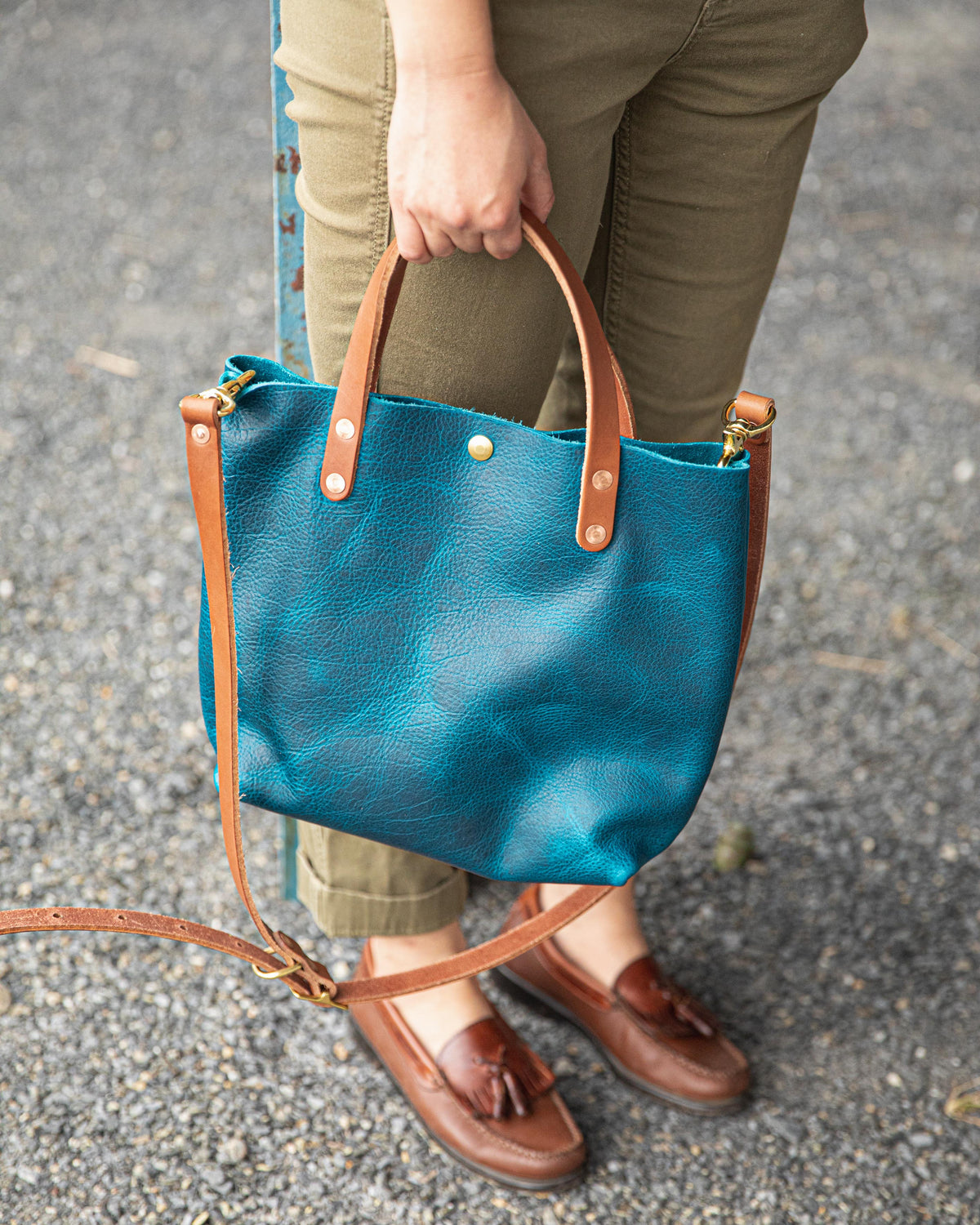 Petrol Blue Bison Mini Tote, a vibrant blue full-grain leather bag with tan handles, held by a person.