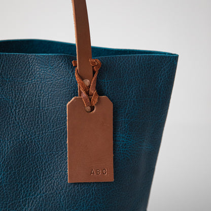 Petrol Blue Bison leather tote bag featuring a vibrant natural grain and a customizable tan leather luggage tag.