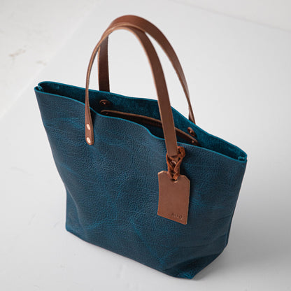Handmade Petrol Blue Bison leather tote bag featuring a rich natural grain, durable tan handles, and a custom embossed tag.