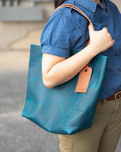 Handmade Petrol Blue Bison leather tote bag with natural grain and tan leather handles, worn over the shoulder.