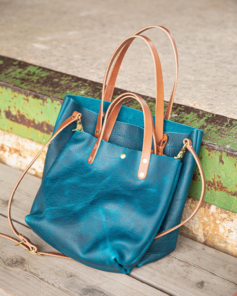 Handmade petrol blue bison leather tote bag featuring a rich natural grain, durable tan leather handles, and brass hardware.
