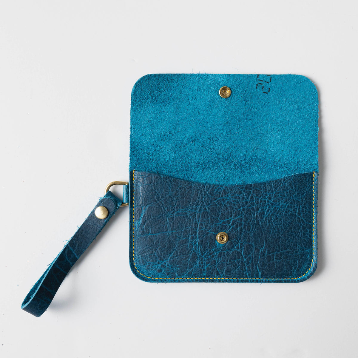 Petrol blue full-grain leather wristlet clutch, open to reveal a bright blue interior and brass hardware.
