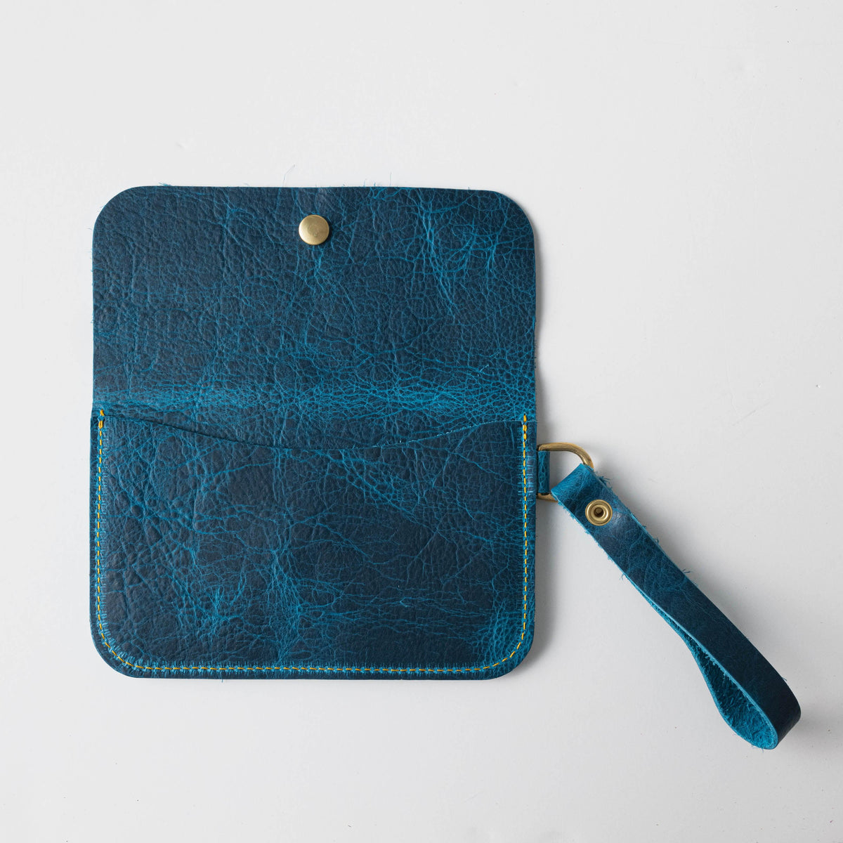 Open petrol blue full-grain leather wristlet clutch with brass snap, yellow stitching, and strap.