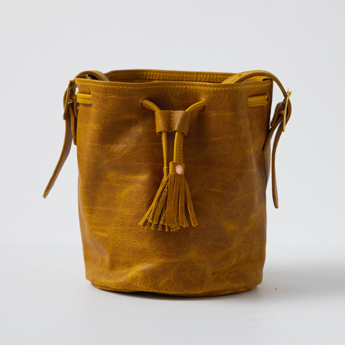 Vibrant Yellow Bison full-grain leather bucket bag with prominent grain, soft temper, and drawstring tassel closure.