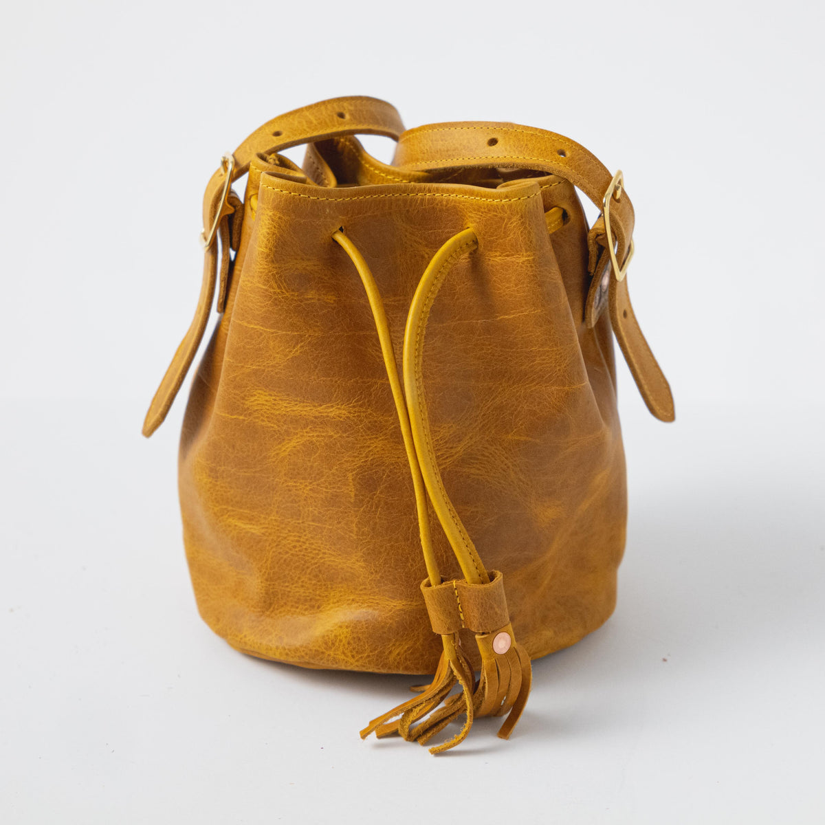 Vibrant Yellow Bison full-grain leather bucket bag with prominent grain, drawstring closure, and tassel detail.