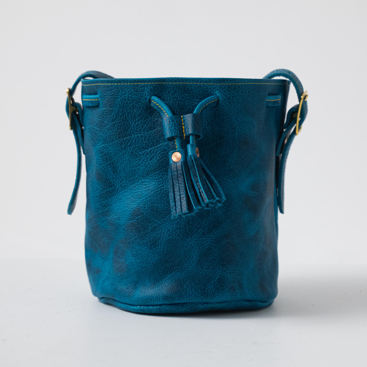 Petrol Blue Bison Bucket Bag: handcrafted leather with drawstring closure, playful tassels, and elegant gold hardware.