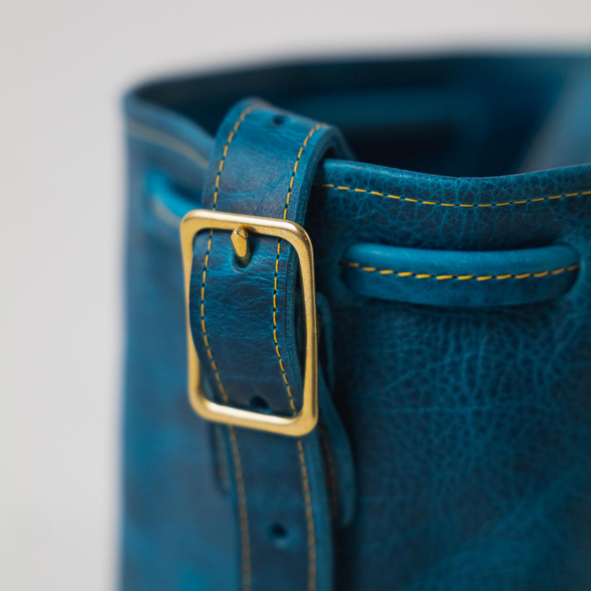 Petrol Blue Bison Bucket Bag with elegant leather drawstring closure, playful tassels, and brass buckle.