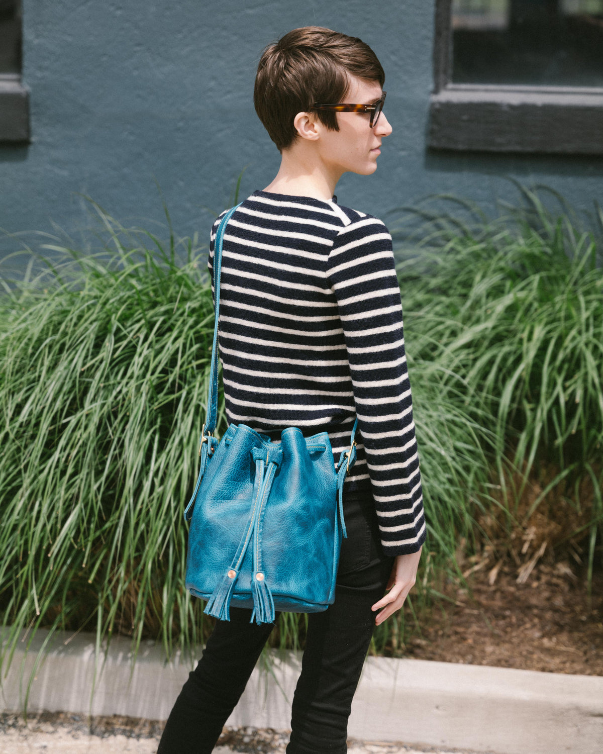 Petrol Blue Bison Bucket Bag with elegant leather tassels, worn crossbody by a person in a striped sweater.